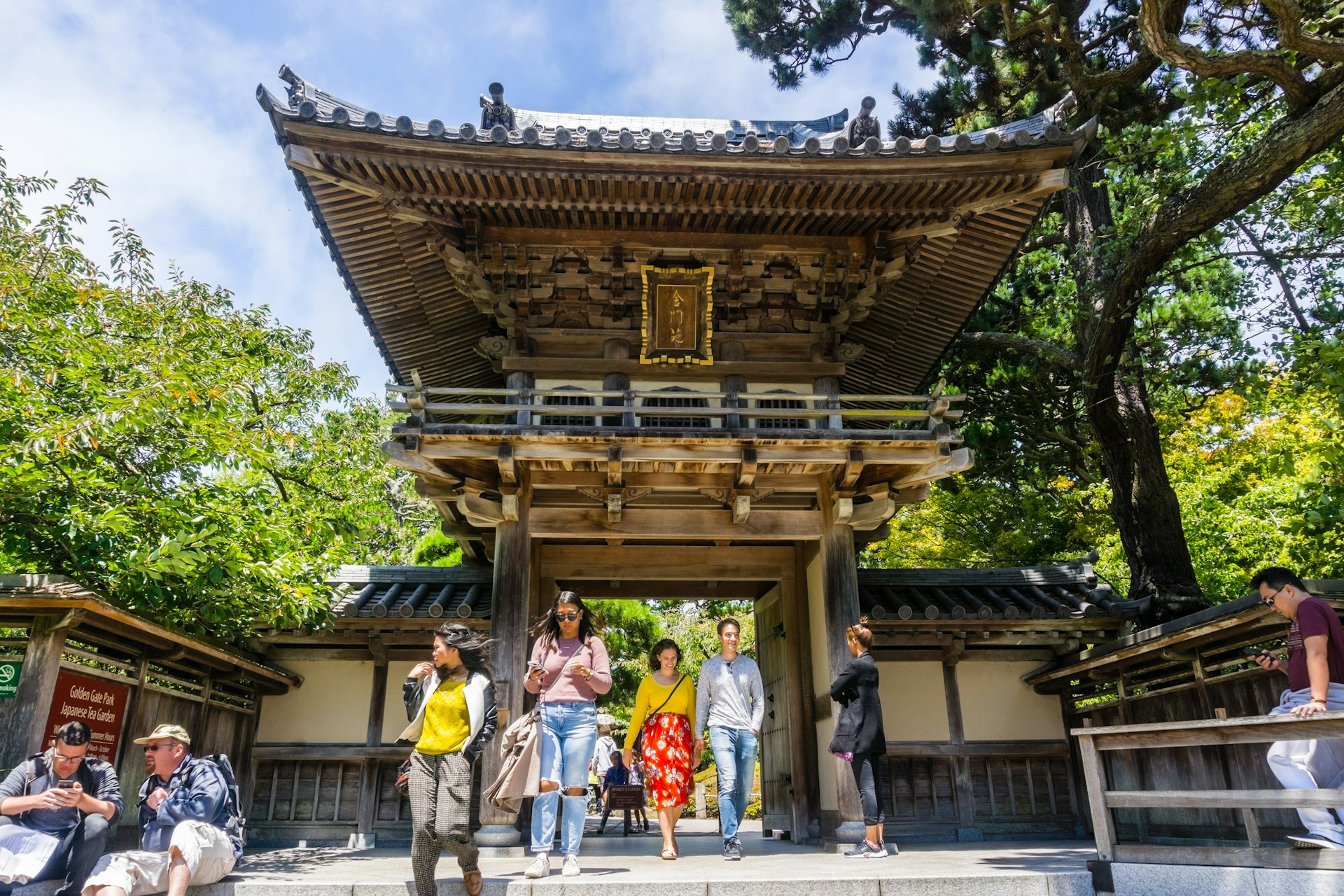 A wooden gateway marks the entrance to a Japanese Tea Garden. Tourists are milling around out front 